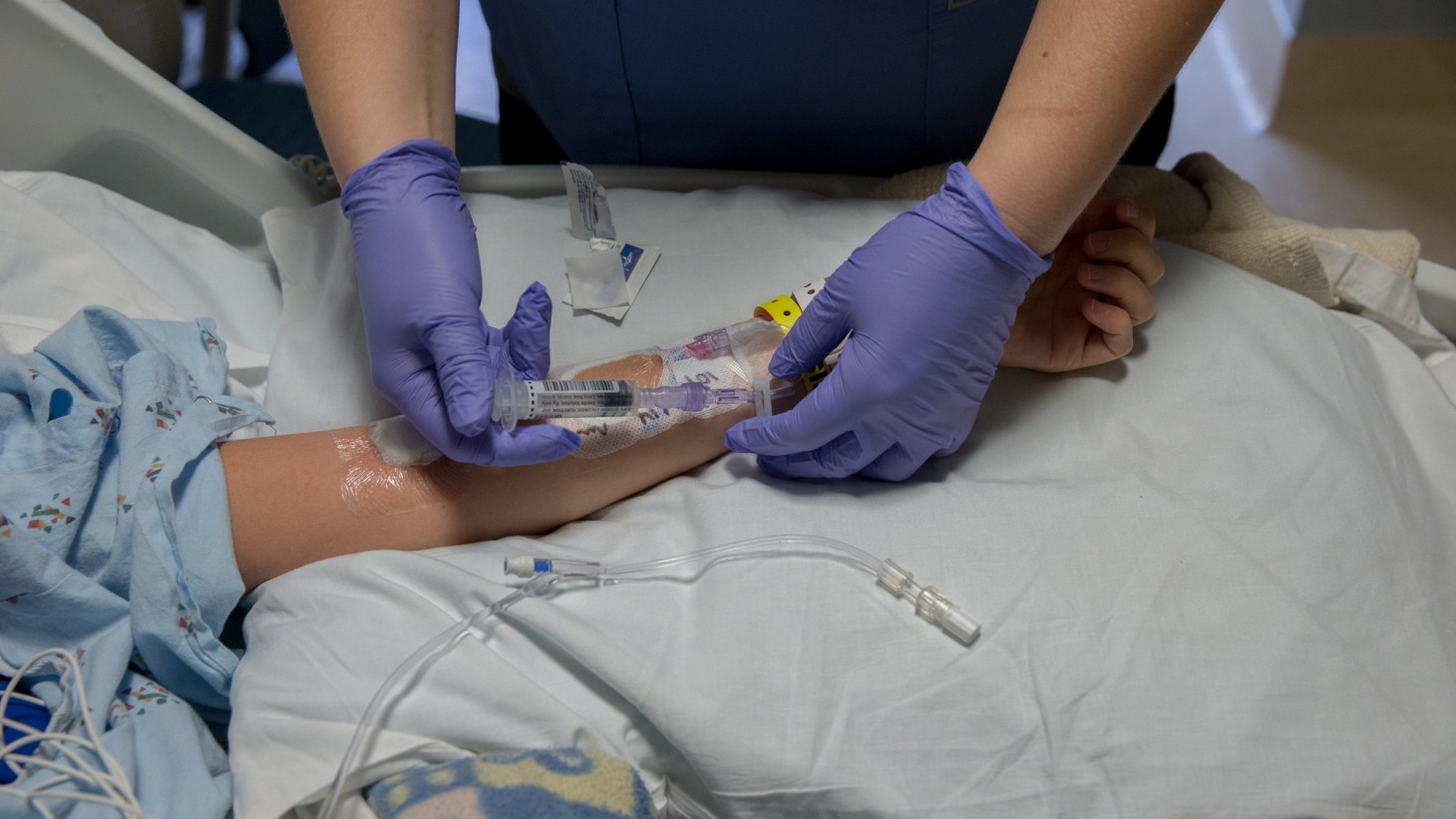 A pair of hands inserting an IV in a patient's arm 